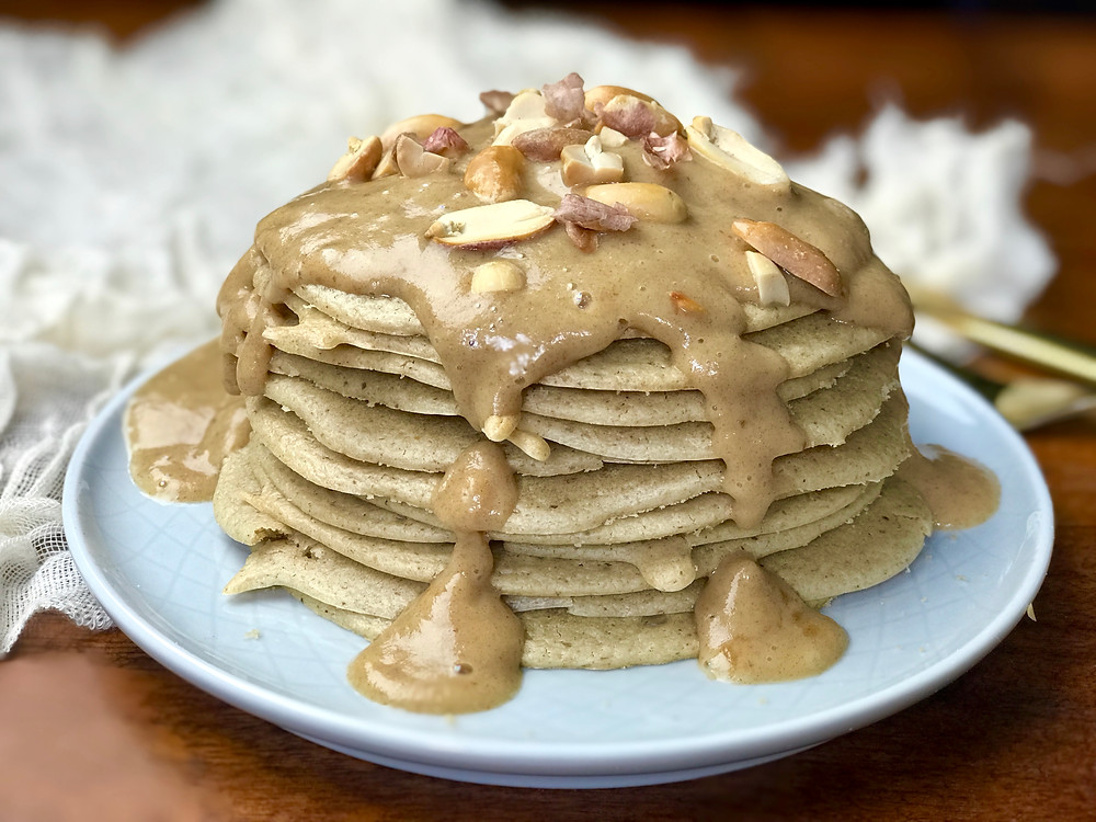 Golden baked vegan peanut butter pancakes stacked high with peanut butter date syrup dripping down