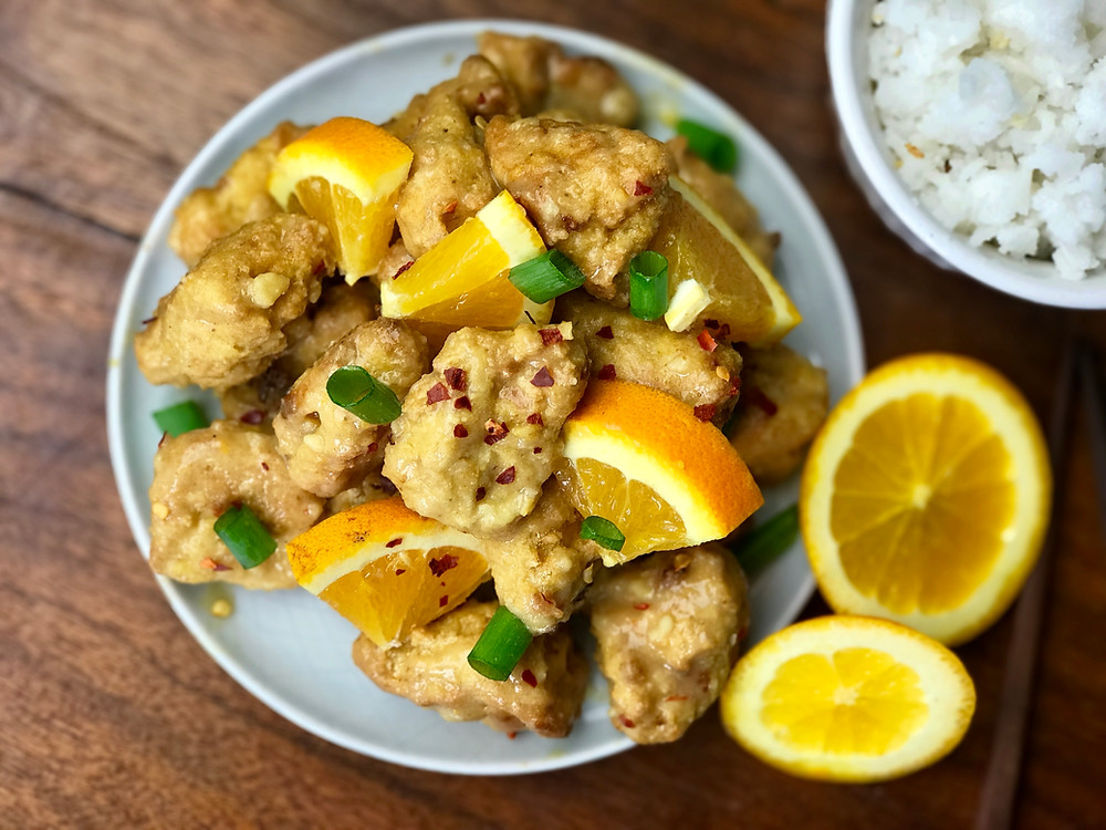 Crispy golden air fried orange tofu pieces coated in glossy orange sauce with green onion garnish